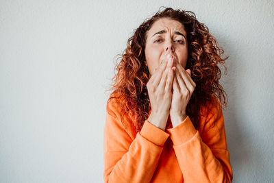 Woman sneezing while standing against wall