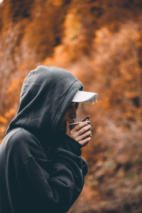 Young woman having drink while standing against trees during autumn