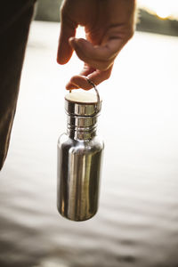 Midsection of man holding bottle standing by lake during vacation