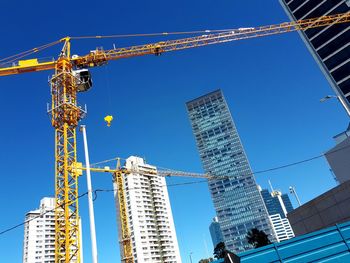 Low angle view of crane by building against clear sky