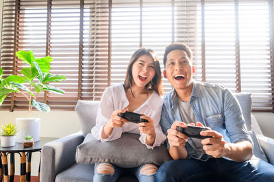 Smiling couple playing video game while sitting on sofa at home