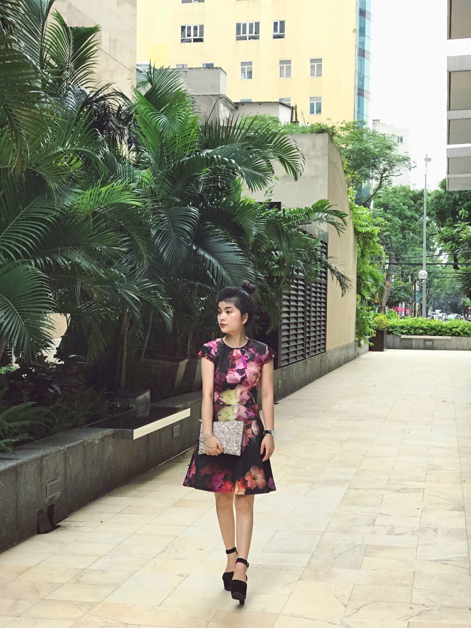 one person, front view, real people, outdoors, smiling, looking at camera, young adult, full length, day, built structure, young women, lifestyles, architecture, portrait, standing, beautiful woman, tree, building exterior, happiness, palm tree, growth, medium-length hair, city, people