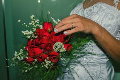 Midsection of bride holding red rose bouquet