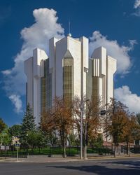 Trees by modern buildings against sky