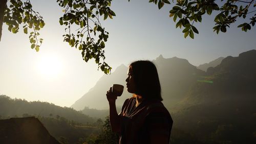 Woman drinking coffee by mountains against sky