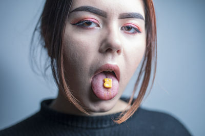 Portrait of woman licking candy against gray background