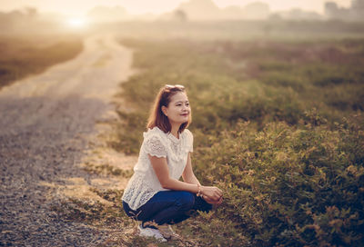 Woman crouching on field against sky during sunset