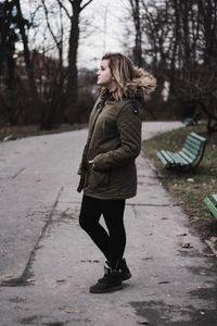 Side view of young woman standing on walkway at park during winter