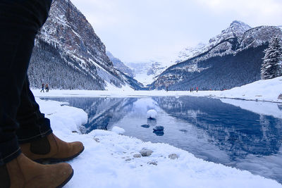 Low section of person standing by lake during winter against mountains