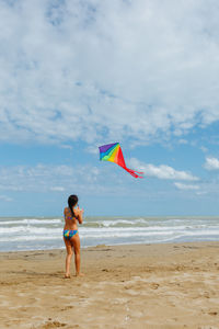 Rear view of woman standing at beach against sky