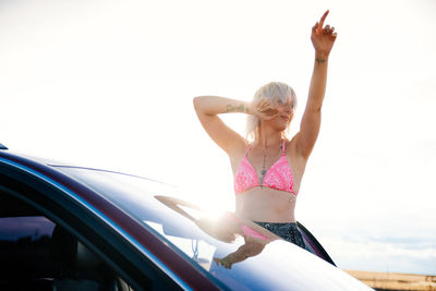 Young woman dancing outside her car in a bikini in the sun