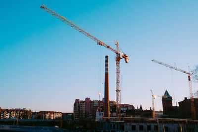Cranes in city against clear sky