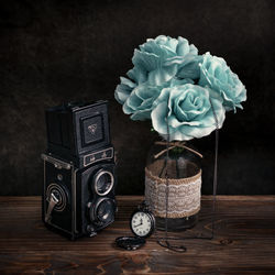 Close-up of camera and pocket watch with turquoise flowers on table