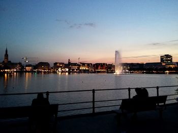 Rear view of silhouette buildings in front of calm sea at dusk