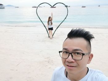Portrait of man with girlfriend standing amidst heart shape at beach