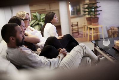 Family watching tv while sitting on sofa in living room at home