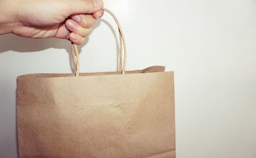 Cropped image of hand holding paper bag against wall