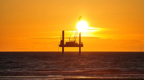 Silhouette of a sea platform on sea against orange sky