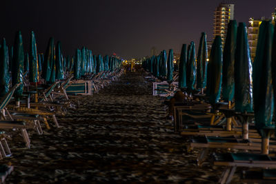 Row of deck chairs and closed parasol at beach against sky