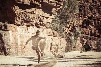 Man dancing on sand against rock formations during sunny day