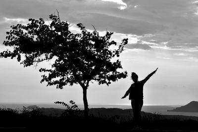 Silhouette man standing by tree on field against sky