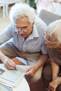 High angle view of senior couple doing crossword puzzle in newspaper at nursing home