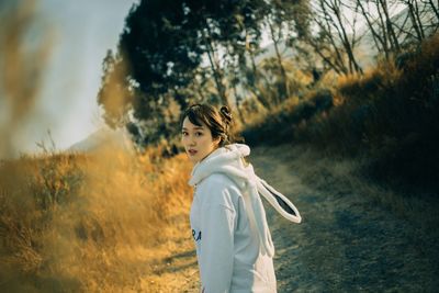 Portrait of woman standing on field against trees during sunset