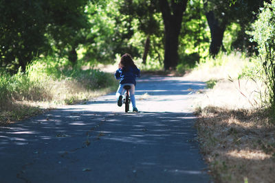 Rear view full length of girl riding bicycle on road