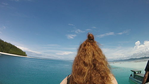 Rear view of woman standing at shore against sky