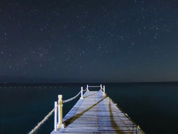 Pier over sea against star field at night