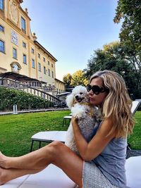 Side view of mature woman playing with dog while lying on chair against building