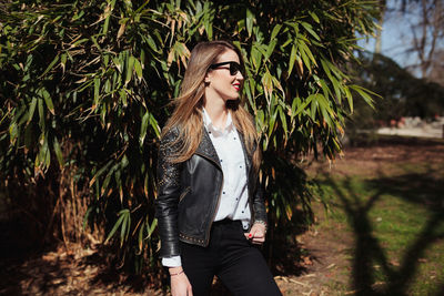 Smiling young woman wearing sunglasses while standing against plants in park