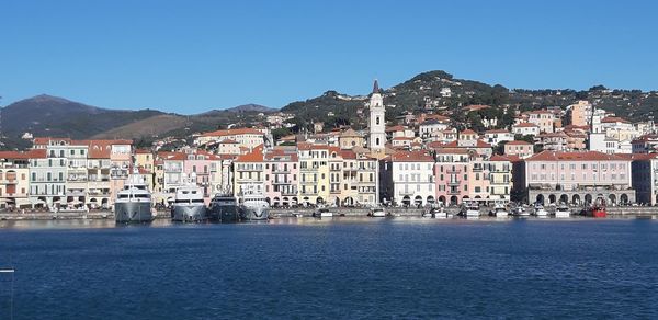 Buildings by sea against clear blue sky