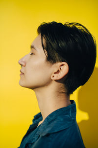 Side view of young woman against yellow background