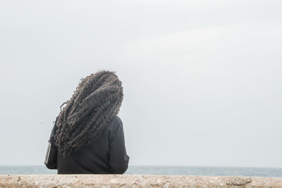 Rear view of woman with curly hair standing at beach against clear sky