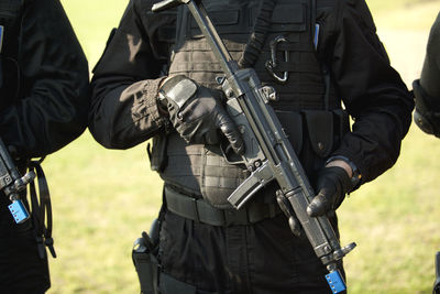 Midsection of army soldiers holding guns on field