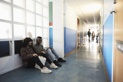 Friends using digital tablet while students standing in corridor at university