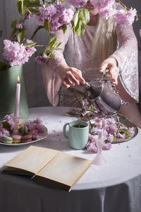 Young woman pours coffee into a cup on a background of sakura flowers and colored macaroon cakes, 