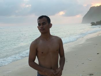 Shirtless young man standing on shore at beach