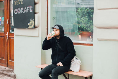 Man drinking coffee in cup while sitting on bench