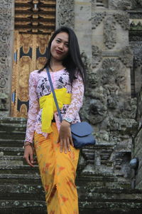 Portrait of smiling young woman standing against building