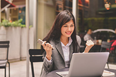 Businesswoman clenching fist while using laptop in cafe