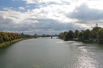 Scenic view of calm river in city against cloudy sky