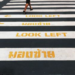 Low section of woman walking on zebra crossing road sign