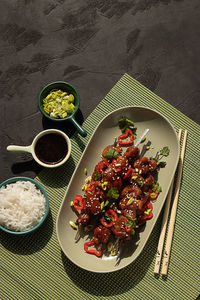 Top view of delicious marinated chicken on skewers topped with greens served on table with bowls of rice, soy sauce and leek in restaurant