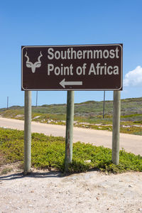 Information sign on road by field against sky