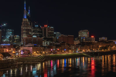 Illuminated buildings by river against sky at night