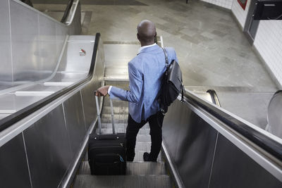 High angle rear view of businessman standing with luggage on escalator at subway station