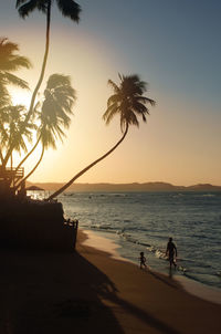 Silhouette people on beach against sky during sunset