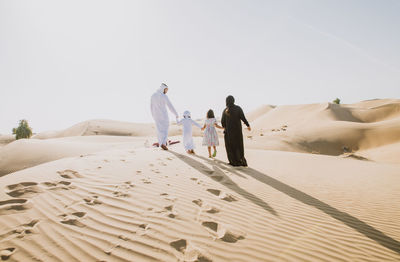 Rear view of people walking on sand dune